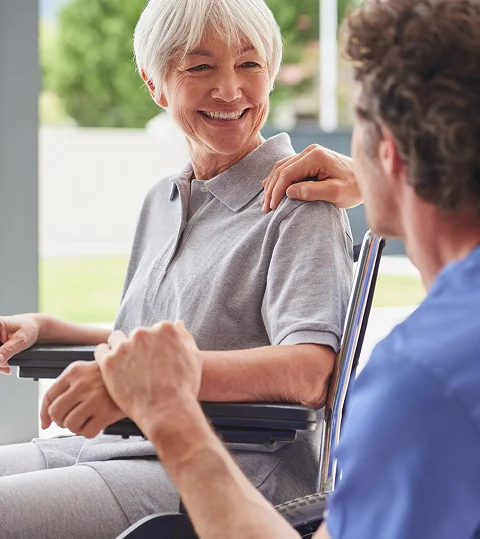 Smiling elderly woman in wheelchair interacting with a caregiver