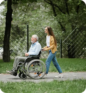 Young caregiver walking with elderly man in a wheelchair outdoors