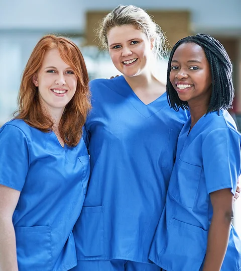 Three smiling nurses in blue scrubs standing together