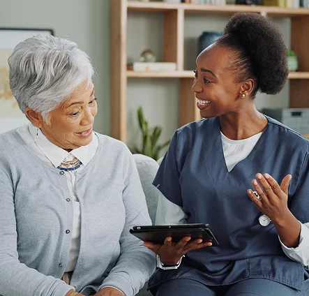 Caregiver in scrubs discussing care plan with an elderly woman using a tablet