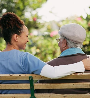Companion caregiver sitting with elderly woman on park bench providing emotional support