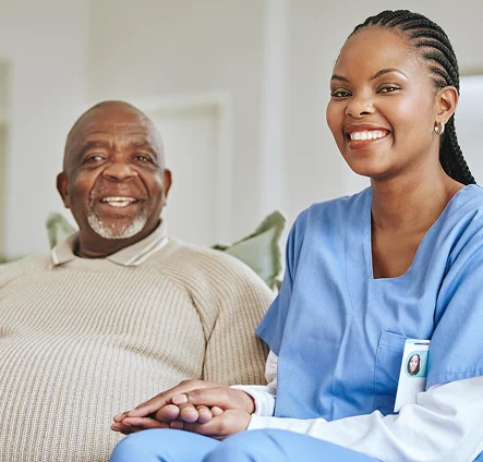 Female nurse holding hands with a smiling elderly male patient on a couch