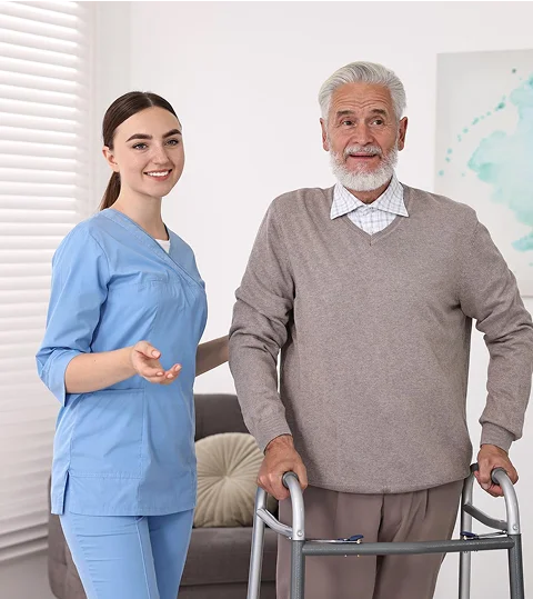 A caregiver standing beside a smiling elderly man using a walker indoors
