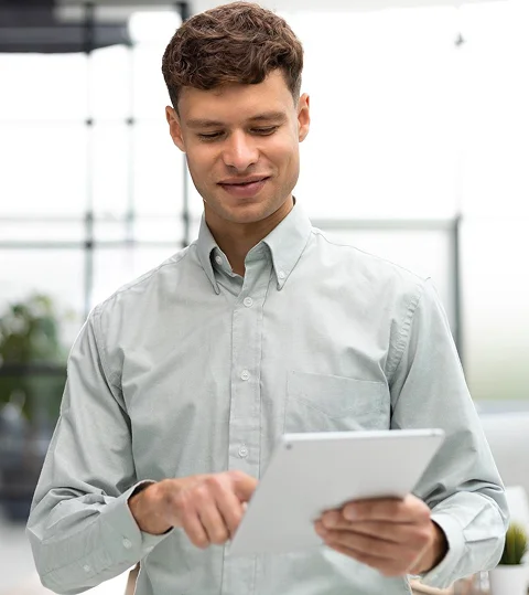 A young professional man smiling while using a tablet in an office