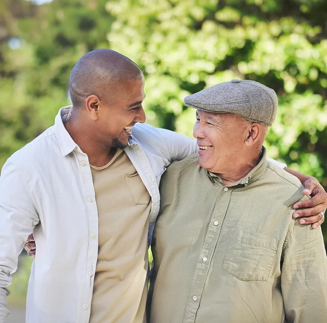 A younger man and older man smiling and walking together with arms around each other outdoors